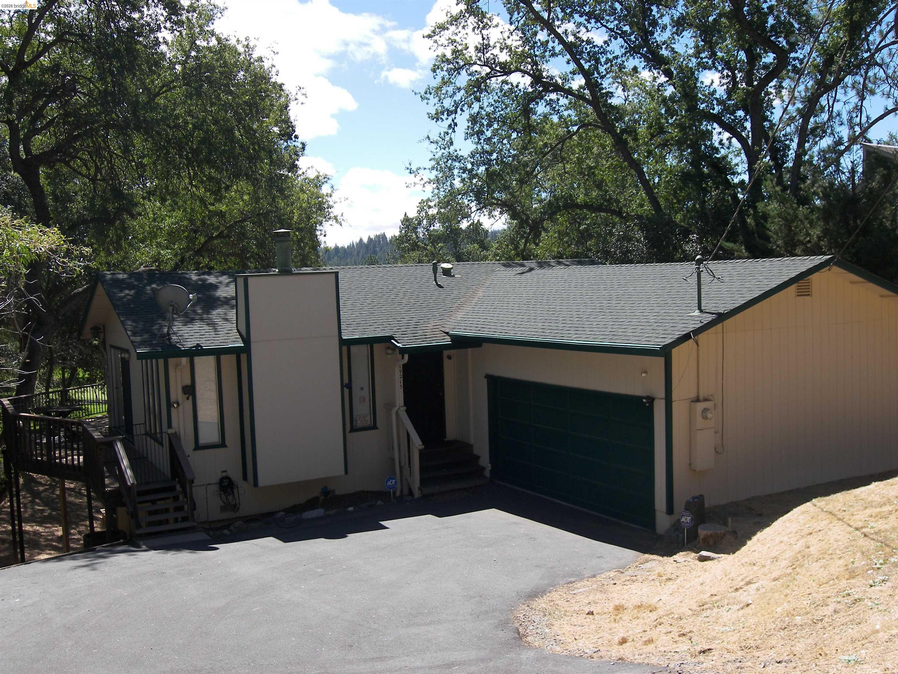 19215 Ferretti Road Groveland, CA 95321 - Photo 2 of 40 Single-story residence featuring a dark green garage door, a paved driveway, and an exterior deck with railing