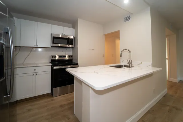 a kitchen with stainless steel appliances a sink dishwasher a stove top oven a refrigerator with white cabinets and wooden floor