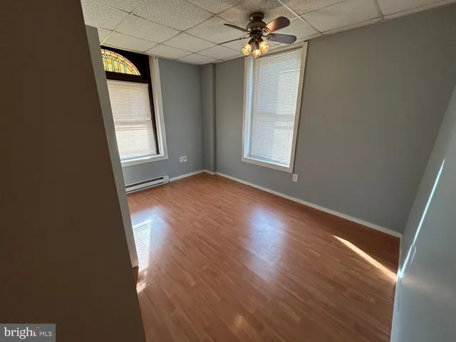 an empty room with wooden floor chandelier fan and windows