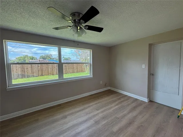 an empty room with wooden floor fan and windows