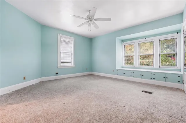 an empty room with chandelier fan and windows