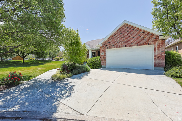 31 Village Square Road Centerville, UT 84014 - Photo 4 of 29 Brick facade residence featuring an attached garage with a white door, a concrete driveway, established landscaping, and mature trees