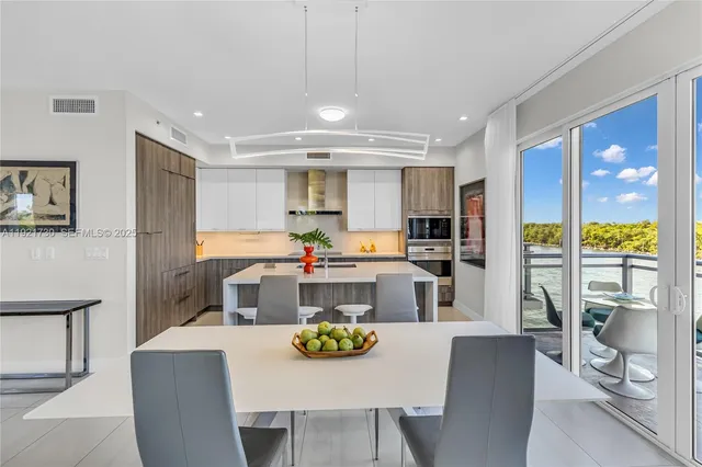 a kitchen with stainless steel appliances kitchen island granite countertop a dining table chairs and a refrigerator