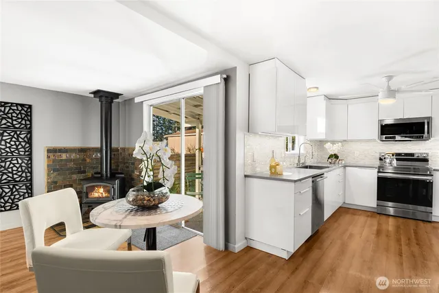 a kitchen with stainless steel appliances kitchen island granite countertop a refrigerator a sink a stove and white cabinets with wooden floor