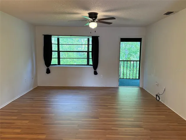 an empty room with wooden floor chandelier fan and windows