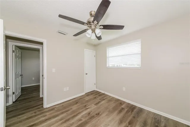 an empty room with wooden floor fan and windows