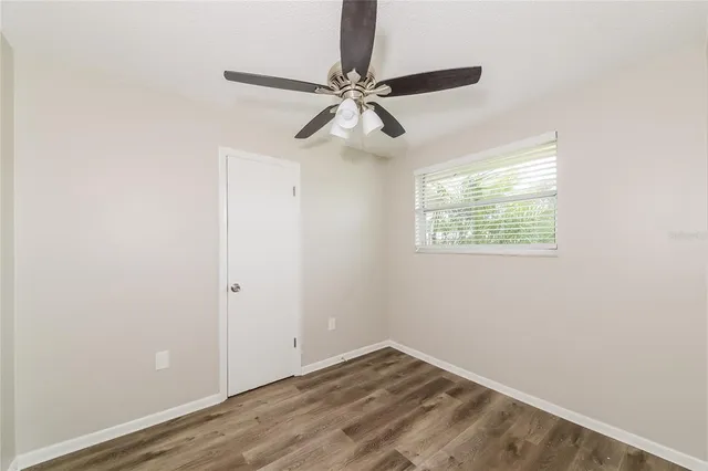a view of an empty room with wooden floor and a ceiling fan