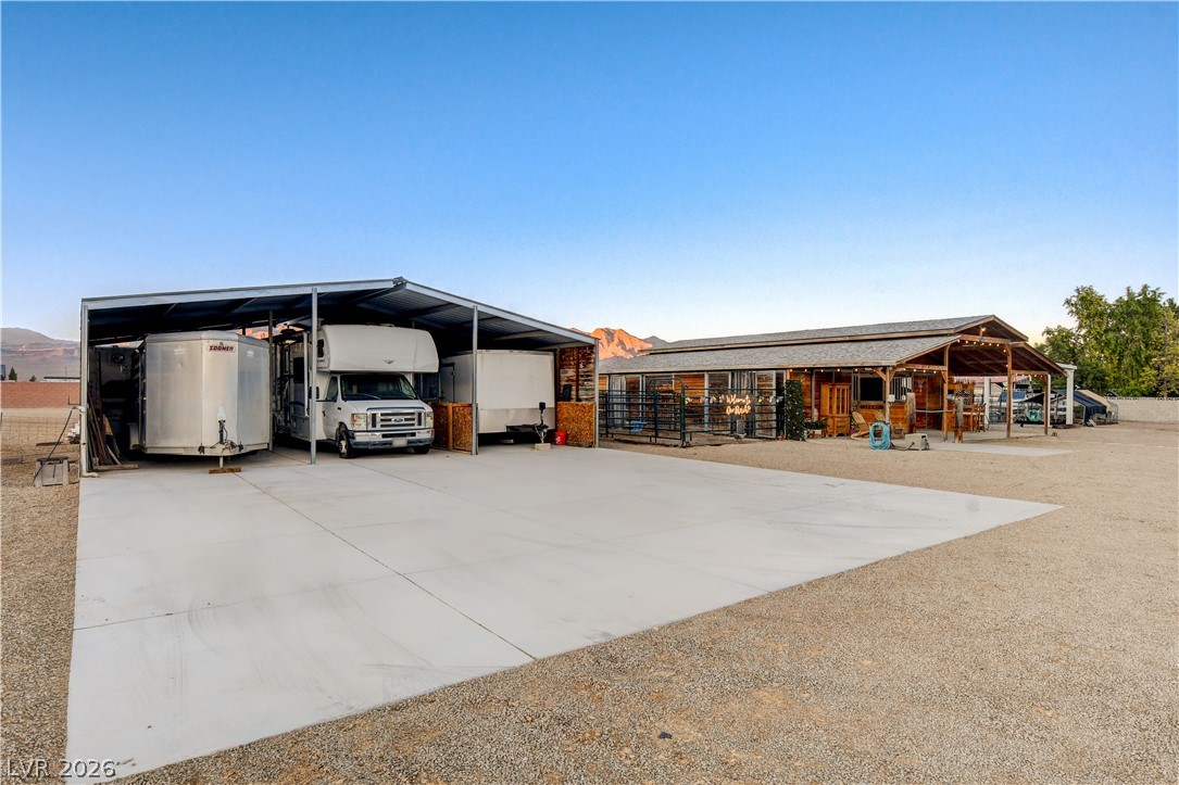 6460 Racel Street Las Vegas, NV 89131 - Photo 30 of 59 A spacious concrete pad fronting covered vehicle storage and an outbuilding under open desert skies.