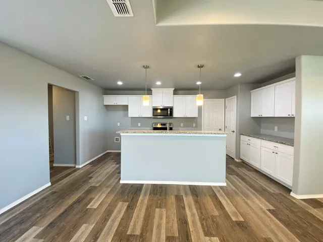 a large kitchen with stainless steel appliances kitchen island a sink dishwasher a refrigerator and white cabinets with wooden floor