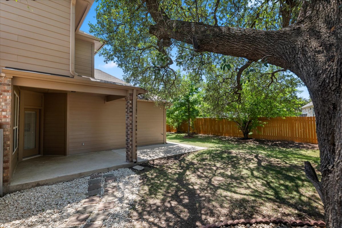 3451 Mayfield Ranch Boulevard, Unit 311 Round Rock, TX 78681 - Photo 37 of 40 Expansive backyard featuring a covered patio, a large mature tree, a wooden privacy fence, a manicured lawn, and a stone-lined gravel path