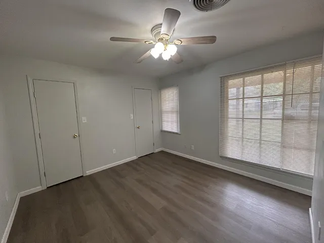 an empty room with wooden floor chandelier fan and windows