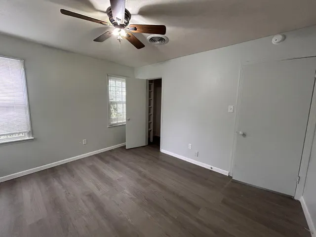 an empty room with wooden floor ceiling fan and windows