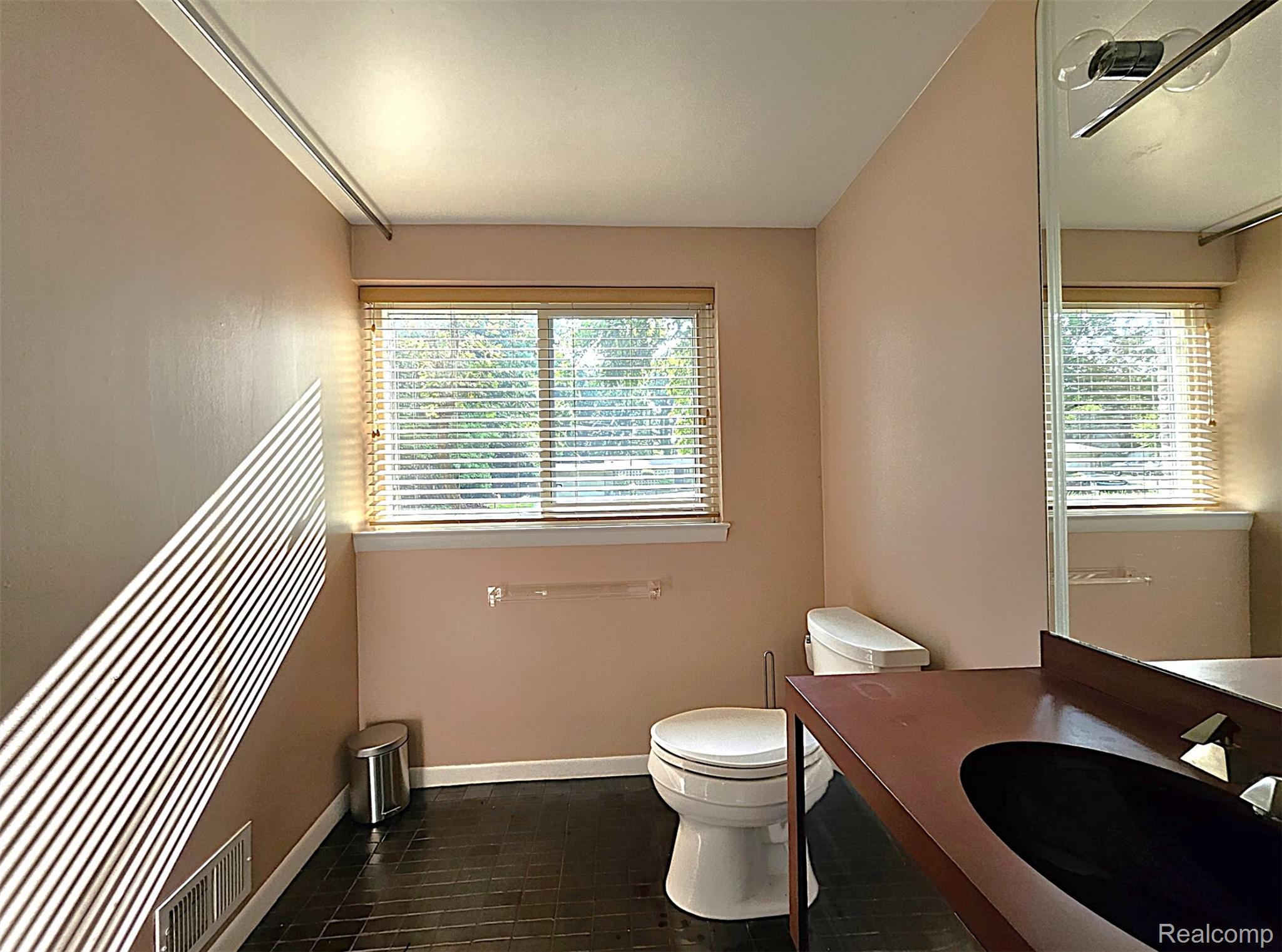 7120 Pebblecreek Road West Bloomfield, MI 48322 - Photo 28 of 31 Bathroom featuring a window with blinds, dark tile flooring, a toilet, a vanity with an integrated dark sink, and a wall-mounted mirror