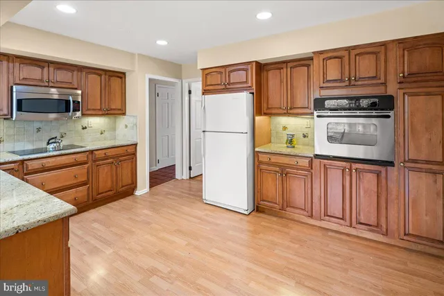 a kitchen with stainless steel appliances granite countertop a refrigerator a stove top oven and a sink with wooden cabinets