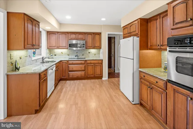 a kitchen with stainless steel appliances granite countertop a refrigerator a sink dishwasher a stove with wooden cabinets and floor