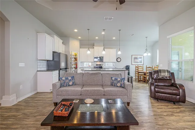 a living room with stainless steel appliances furniture wooden floor and a view of kitchen