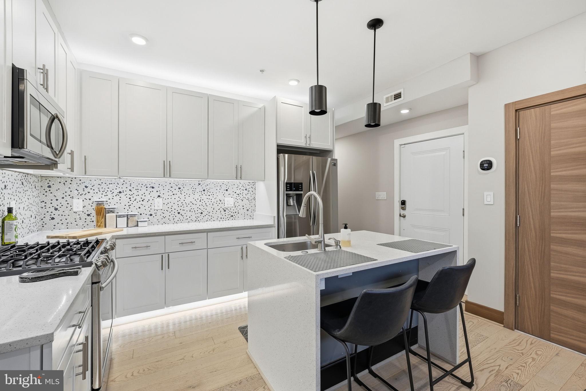 2109 M Street Northeast, Unit 5 Washington, DC 20002 - Photo 3 of 11 a kitchen with stainless steel appliances kitchen island granite countertop a sink a stove a refrigerator and island with wooden floor