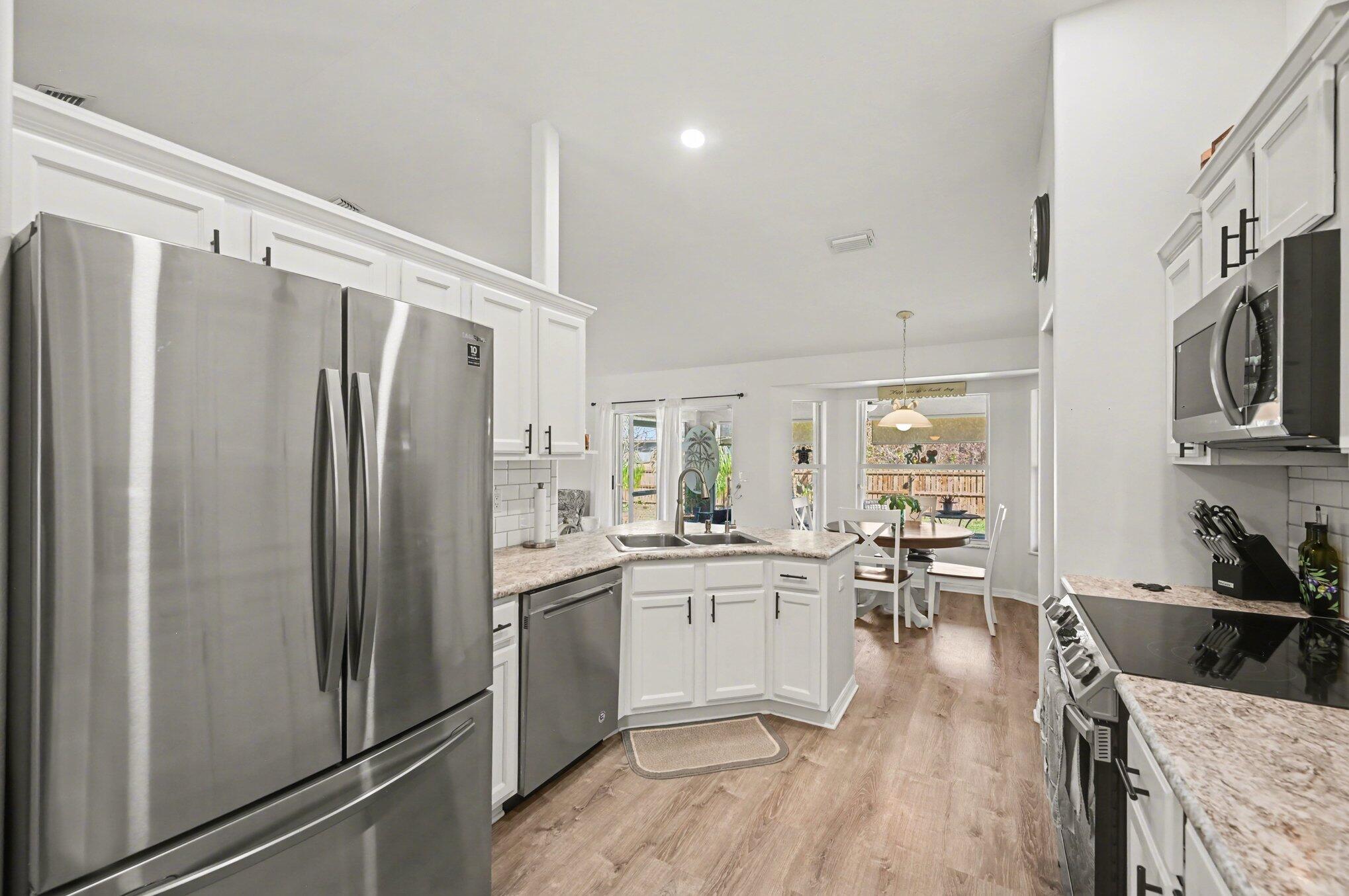 1362 Seahouse Street Sebastian, FL 32958 - Photo 5 of 28 a kitchen with stainless steel appliances a refrigerator a sink dishwasher a stove with white cabinets and wooden floor