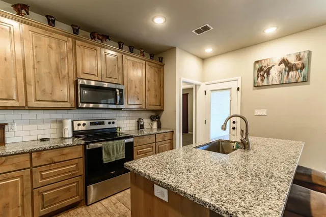 a kitchen with stainless steel appliances granite countertop a stove top oven a sink a refrigerator white cabinets and a dining table