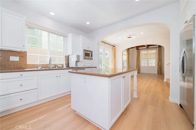 a kitchen with granite countertop a refrigerator a sink and white cabinets