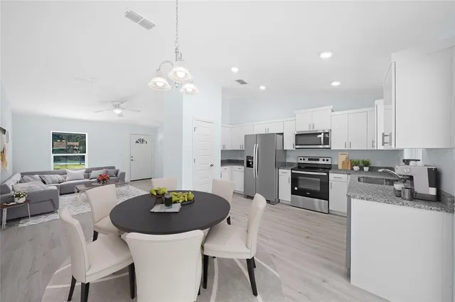 a kitchen with stainless steel appliances kitchen island granite countertop a dining table chairs refrigerator and sink