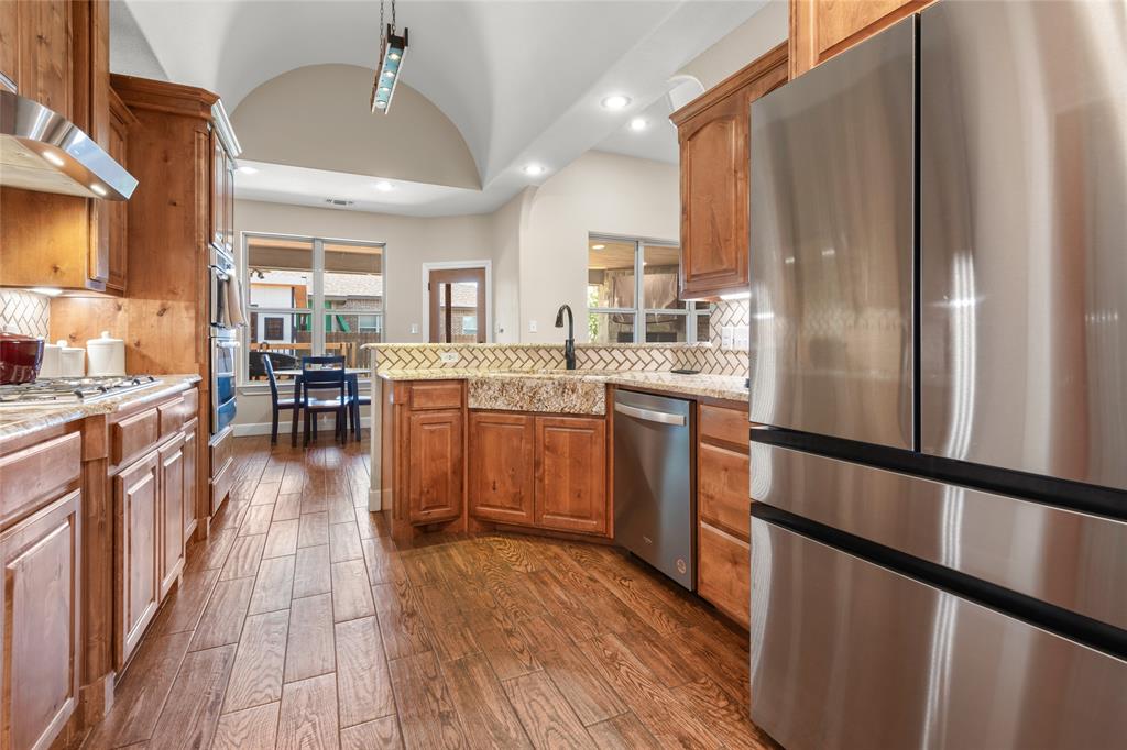 3801 Kady Ridge Abilene, TX 79606 - Photo 13 of 40 Kitchen featuring stainless steel appliances, wood-finish flooring, wood cabinetry, granite countertops, and a tile backsplash