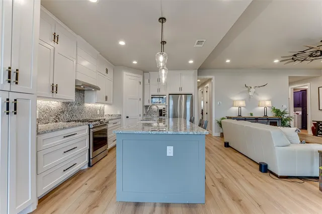 a large kitchen with stainless steel appliances kitchen island granite countertop a stove a sink a refrigerator and white cabinets with wooden floor