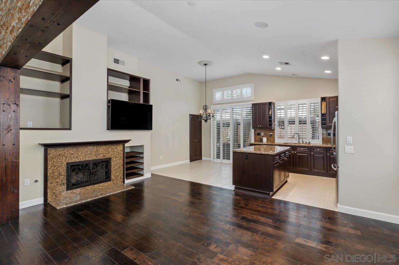 a living room with stainless steel appliances furniture a fireplace a flat screen tv and view kitchen
