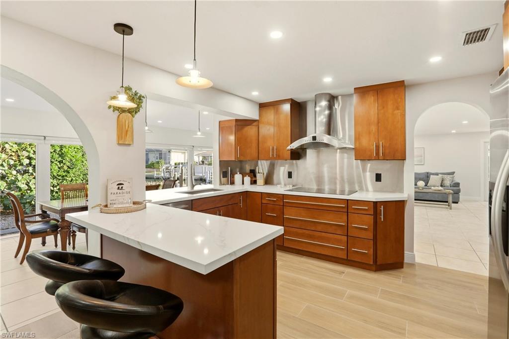 339 Landmark Street Marco Island, FL 34145 - Photo 15 of 50 Kitchen featuring arched walkways, a peninsula, brown cabinets, pendant lighting, and a kitchen breakfast bar