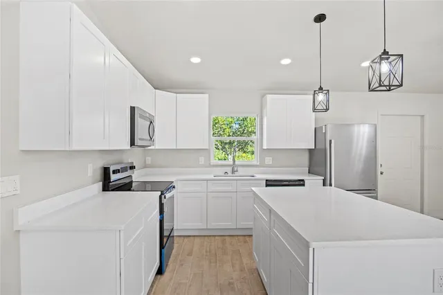 a kitchen with stainless steel appliances a sink a stove a refrigerator and white cabinets