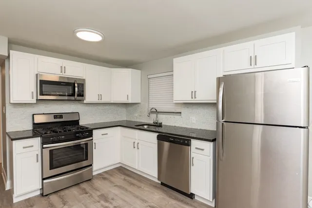 a white kitchen with sink a refrigerator and white cabinets