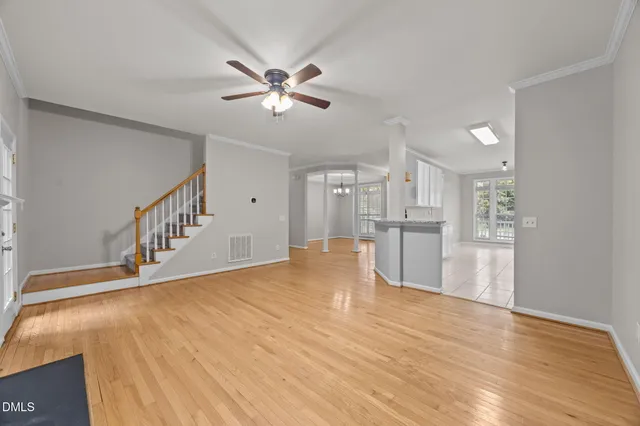 a view of an empty room with wooden floor and a kitchen