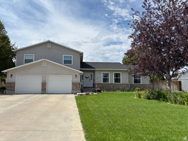 Two-story stucco residence featuring a two-car garage with individual doors, a concrete driveway, and a front lawn with established landscaping
