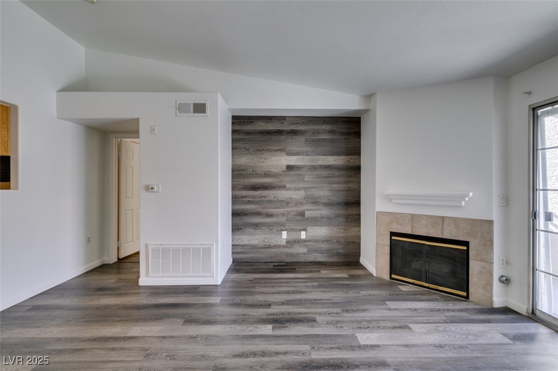 3318 North Decatur Boulevard, Unit 2138 Las Vegas, NV 89130 - Photo 7 of 40 Unfurnished living room featuring a tile fireplace, lofted ceiling, and wood finished floors