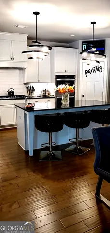 a kitchen with stainless steel appliances kitchen island granite countertop a sink dishwasher a stove and white cabinets with wooden floor