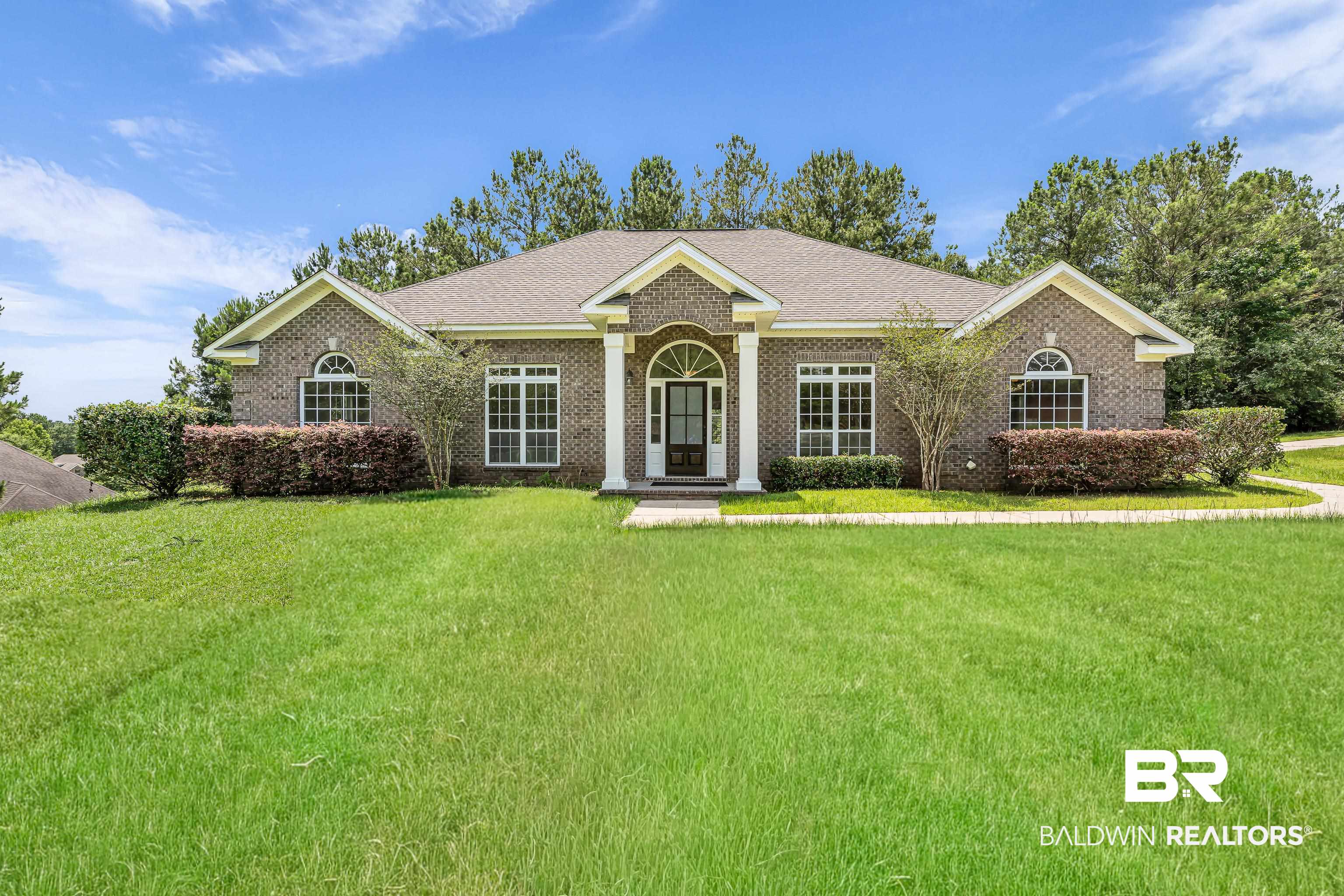 7495 Bromley Road Bay Minette, AL 36507 - Photo 1 of 31 Brick exterior home featuring a columned entry, arched windows, gabled roofline, mature shrubs, and an expansive lawn