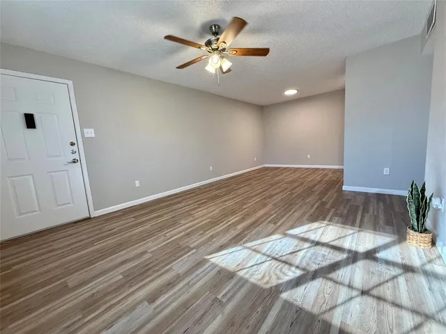 a view of an empty room and chandelier fan and wooden floor