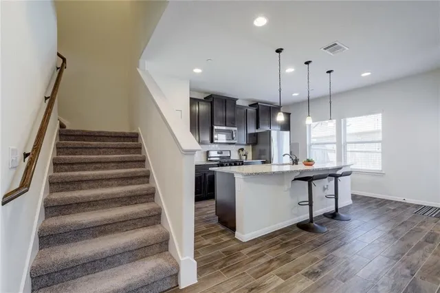 a kitchen with stainless steel appliances granite countertop a refrigerator a sink dishwasher a stove and white cabinets with wooden floor