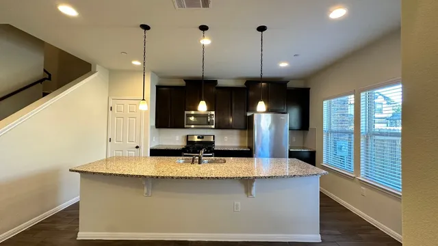 a kitchen with kitchen island granite countertop a sink a counter top space and stainless steel appliances