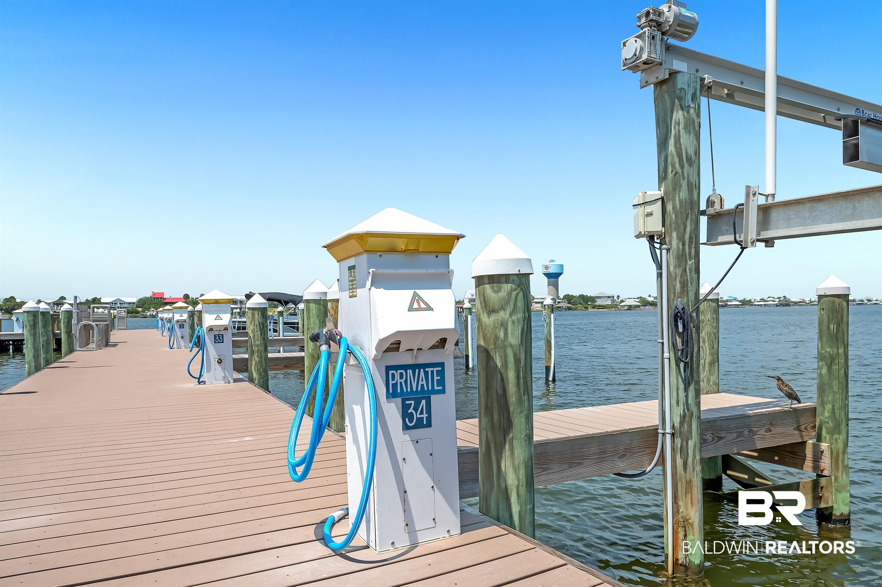 16287 Perdido Key Drive, Unit 105 Pensacola, FL 32507 - Photo 52 of 66 Waterfront dock with composite decking, featuring multiple utility pedestals with hoses, boat lift apparatus, and wooden pilings