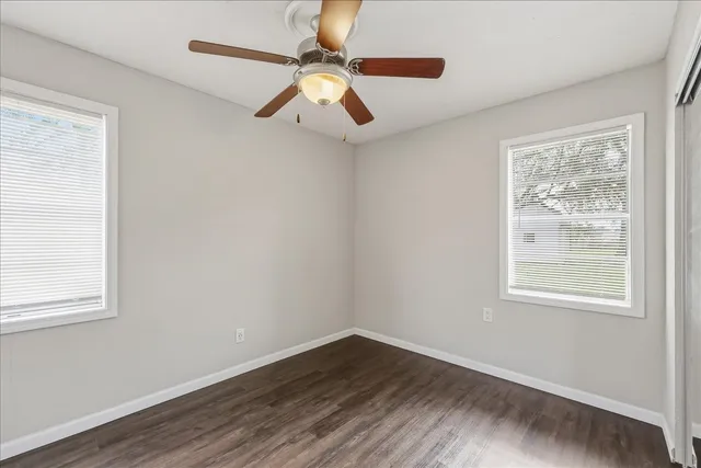 an empty room with wooden floor fan and windows