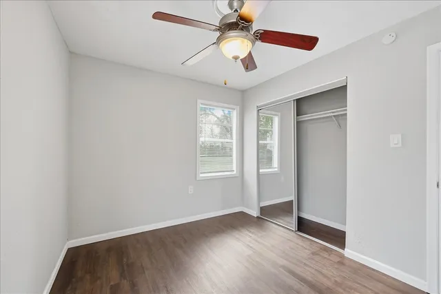 an empty room with wooden floor chandelier fan and windows