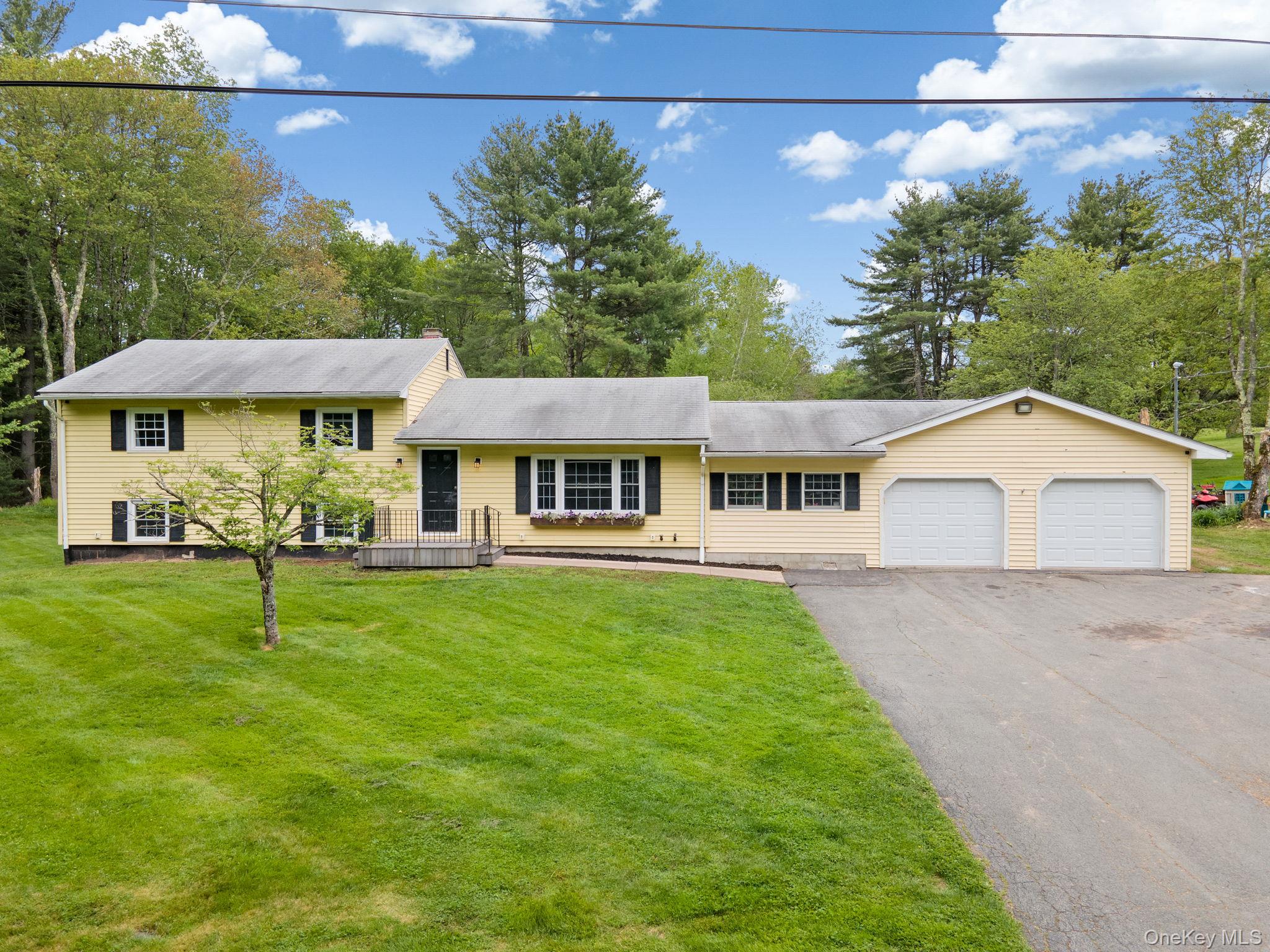 Tri-level home featuring driveway, an attached garage, a front yard, and view of wooded area