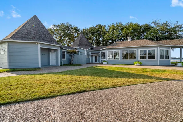 a view of a white house with a big yard and potted plants and large trees