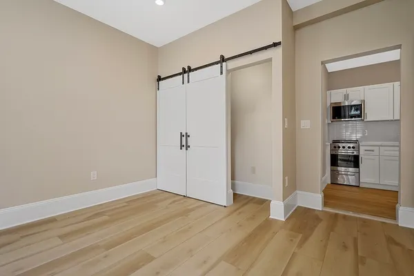 a view of empty room with wooden floor and kitchen
