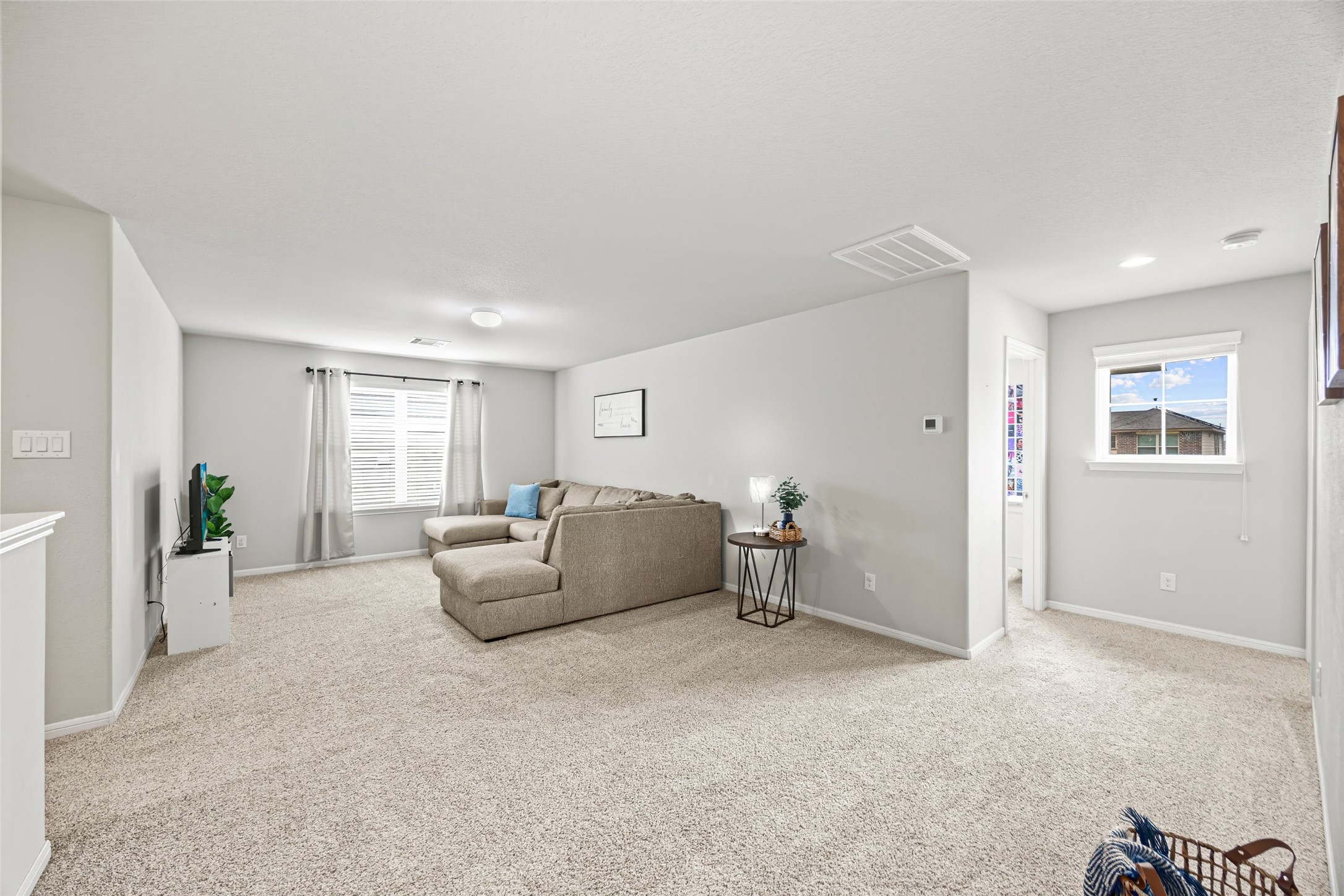 8026 Farthing Lane Rosharon, TX 77583 - Photo 12 of 13 This photo showcases a spacious, carpeted living room with neutral walls and ample natural light from two windows. It features a large sectional sofa and modern decor, creating a cozy and inviting atmosphere.