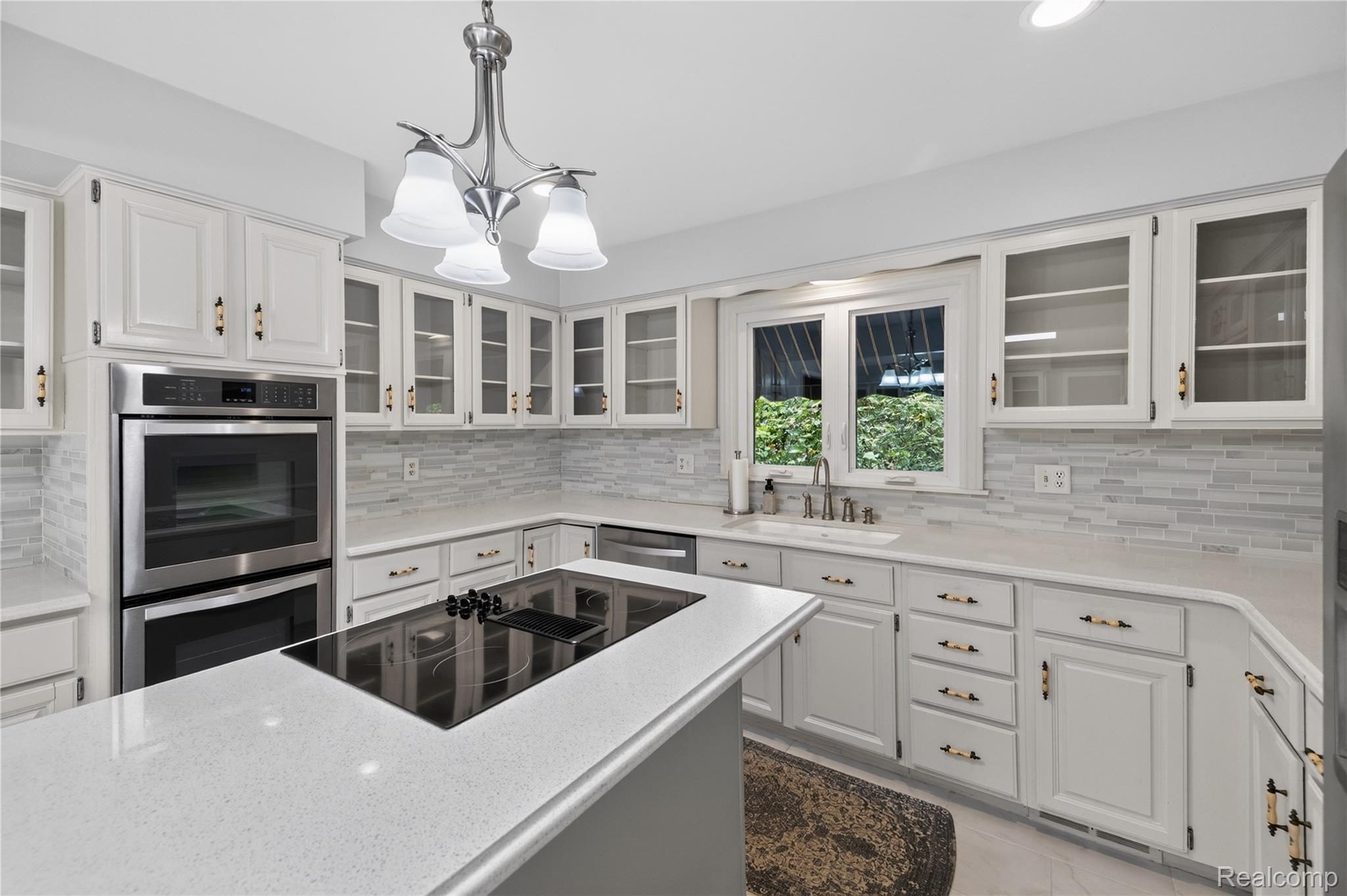 25645 Meridian Road Grosse Ile, MI 48138 - Photo 12 of 46 Kitchen featuring white cabinetry, glass-front upper cabinets, stainless steel double wall ovens, a center island with a cooktop, and light-toned countertops