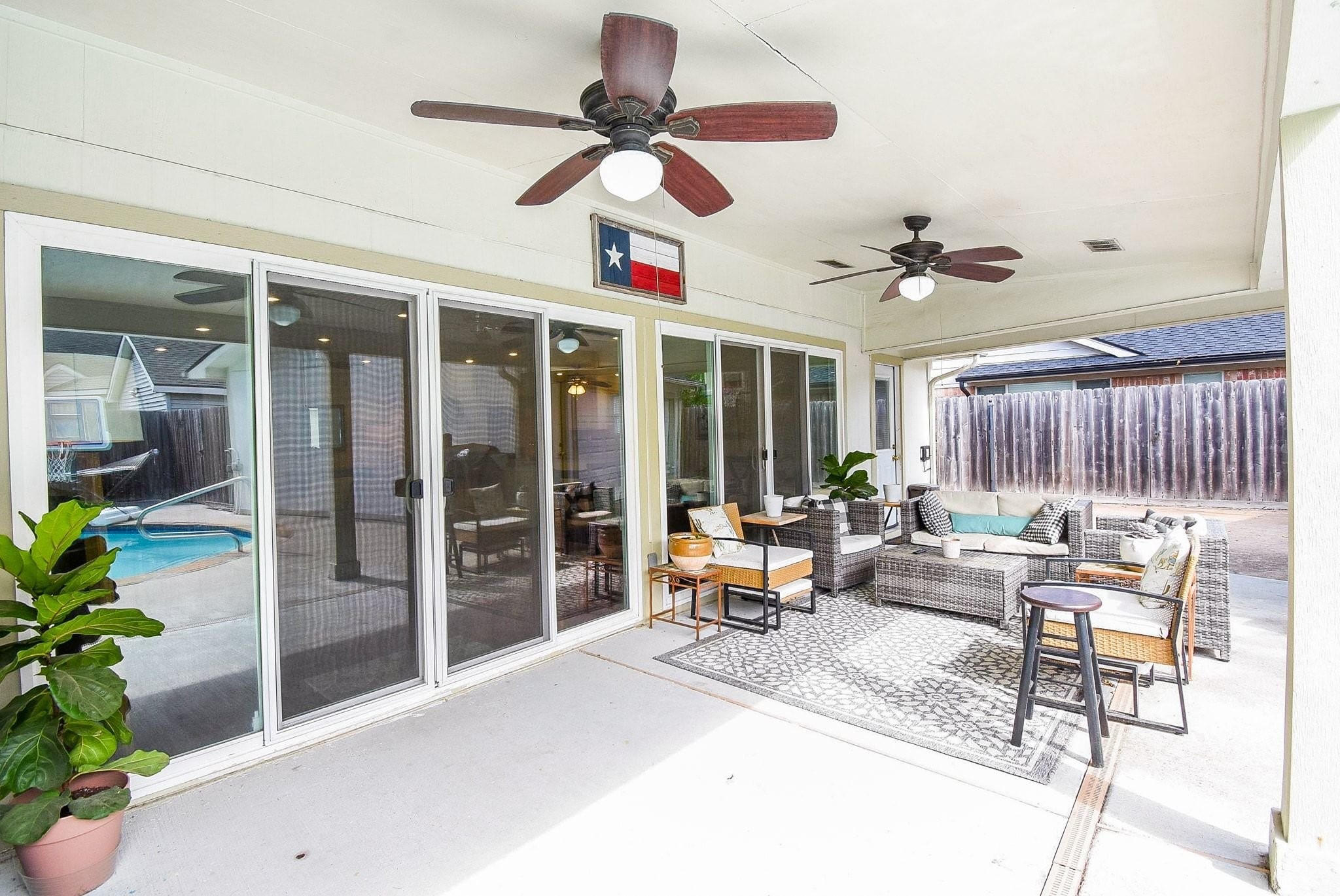 2930 Kevin Lane Houston, TX 77080 - Photo 11 of 50 This photo showcases a spacious covered patio featuring comfortable outdoor seating area, ceiling fans, and sliding glass doors leading to the interior. It's perfect for relaxation and entertaining, with a view of the pool and a privacy fence.