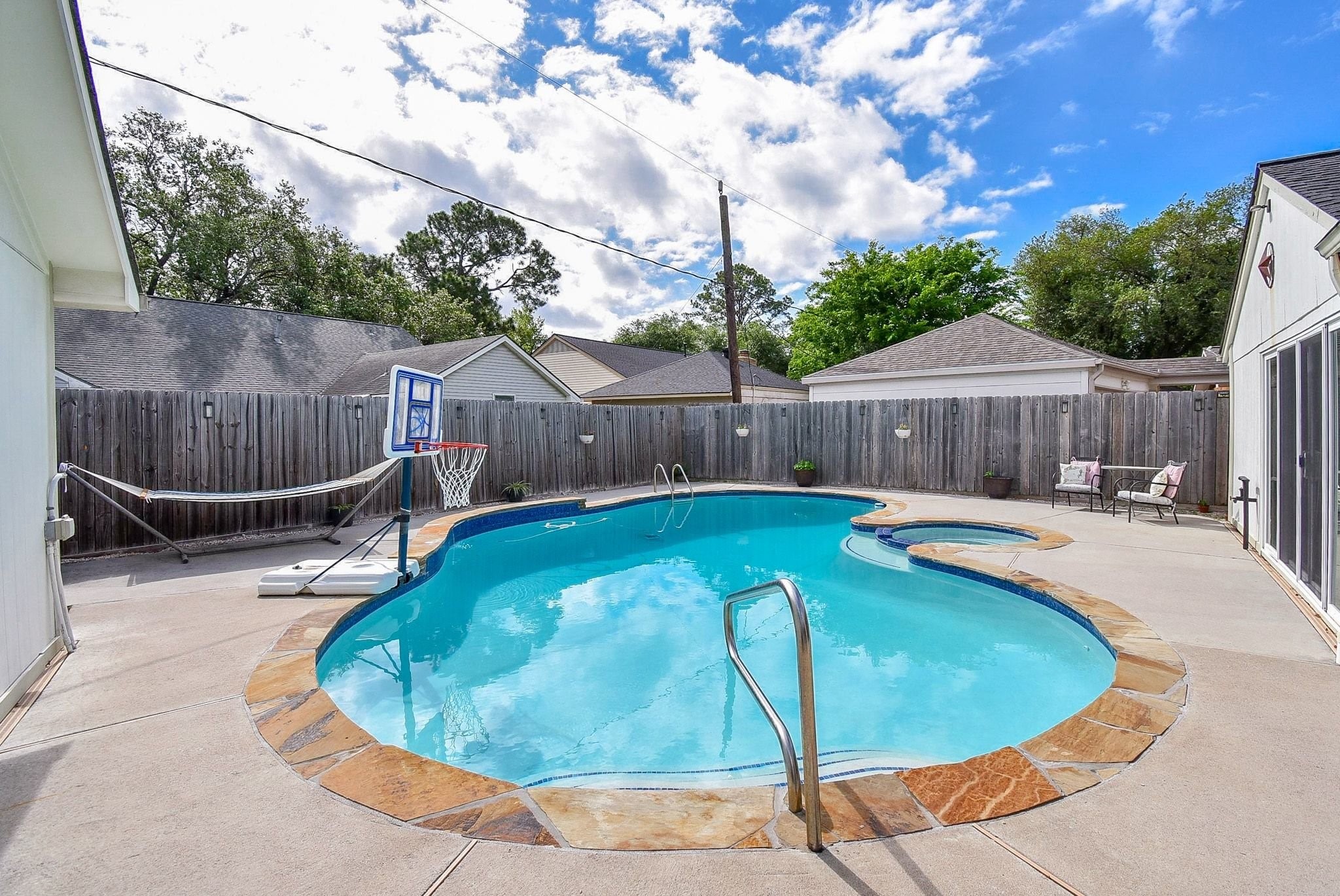 2930 Kevin Lane Houston, TX 77080 - Photo 12 of 50 This backyard features a spacious in-ground pool with a stone border, perfect for relaxation and entertainment. It is surrounded by a privacy fence and has a seating area for outdoor lounging.