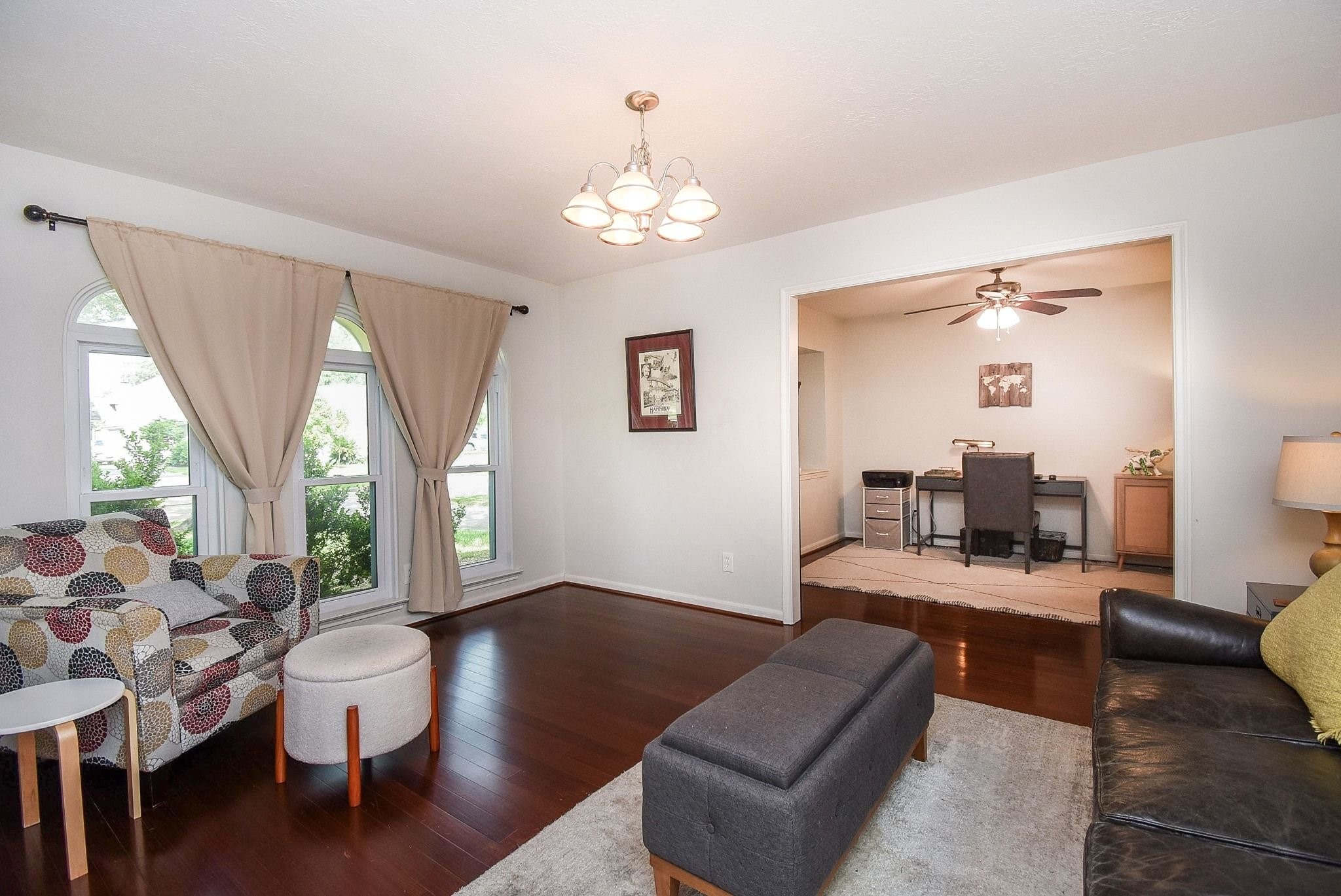 2930 Kevin Lane Houston, TX 77080 - Photo 19 of 50 Bright living room with hardwood floors, featuring a cozy seating area and large windows with elegant drapes. It opens to a home office space with a ceiling fan, perfect for work or study.